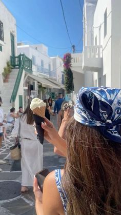 a woman taking a photo of an ice cream cone on the street with other people in the background