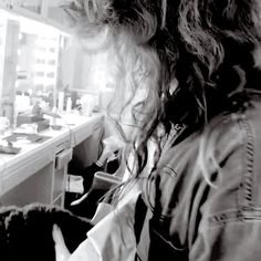 a woman with long hair sitting in front of a counter next to a sink and mirror