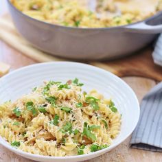 a white bowl filled with pasta and peas on top of a wooden table next to a pot