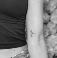 a black and white photo of a woman's arm with a small bird tattoo on it