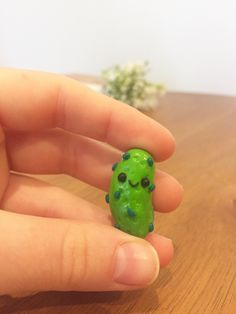 a hand holding a tiny green object on top of a wooden table