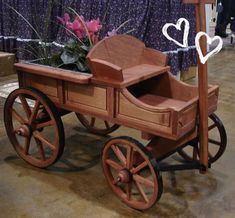 an old fashioned wooden wagon with flowers in it's seat and purple curtains behind it