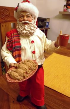 a statue of santa holding a pie on a table with a cup and saucer