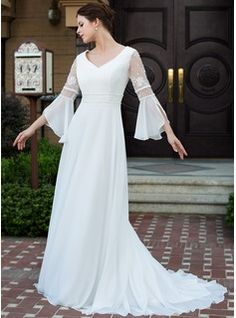 a woman standing in front of a door wearing a white dress with bell sleeves and an open back