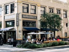 people sitting at tables in front of a restaurant on the corner of a city street