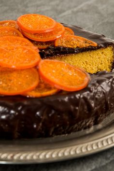 a cake with chocolate frosting and sliced oranges on top, sitting on a plate