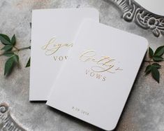 two white cards with gold foil on them sitting on top of a silver platter