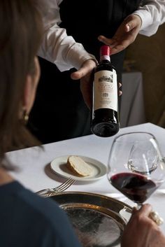 a man pouring red wine into a glass at a table with bread and wine glasses