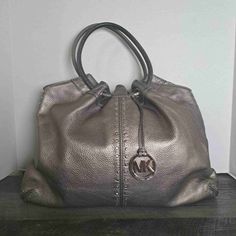 Like New Michael Kors Metallic Pewter Double Handle Logo Charm Handbag Size Extra Large This Michael Kors Tote Is A Stunning Accessory, Featuring A Pebbled Leather Exterior In Metallic Pewter And Accented With A Tasteful Logo Charm. The Double Handles Make For Comfortable Carrying, And Its Spacious Interior Can Hold All Your Essentials. Whether You're Heading To The Office, Shopping, Or Out For The Evening, This Handbag Is Sure To Make A Statement. Size: Womens Extra Large Condition: Like New Co Metallic Shoulder Bag With Silver-tone Hardware For Shopping, Michael Kors Top Handle Shoulder Bag With Silver-tone Hardware, Metallic Leather Shoulder Bag With Silver-tone Hardware, Metallic Tote Shoulder Bag With Silver-tone Hardware, Luxury Tote Shoulder Bag With Silver-tone Hardware, Michael Kors Bag, Pebbled Leather, Fashion Handbags, Tote Handbags