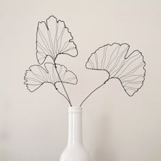 a white vase with two flowers in it sitting on a table next to a wall