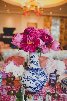 a blue and white vase filled with pink flowers on top of a red table cloth