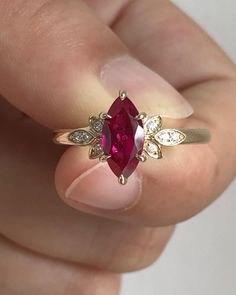 a woman's hand holding a ring with a red stone and diamonds on it