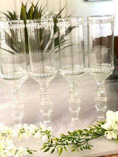 four wine glasses sitting on top of a table next to white flowers and greenery