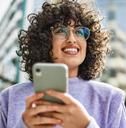 a woman with curly hair is looking at her cell phone while she's smiling