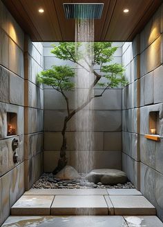 an indoor shower with a tree in the middle and rocks on the ground underneath it