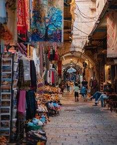 people are walking through an alley way with many items hanging from the ceiling and in front of them