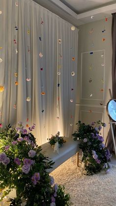 the room is decorated with white curtains and purple flowers on the floor, along with plants