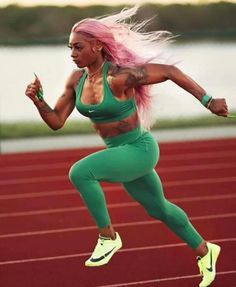 a woman running on a track with pink hair and green leggings in the air