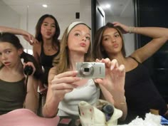 three women taking a selfie in front of a mirror with one holding a camera