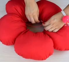 a woman is sewing on a red pillow that looks like a flower ornament