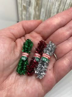 three small tinsel christmas trees in the palm of someone's hand, one is silver and one is red