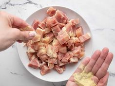 two hands reaching for pieces of raw meat on a white plate with yellow powder in it