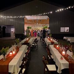 an outdoor dining area with long tables and candles lit up at night, surrounded by string lights