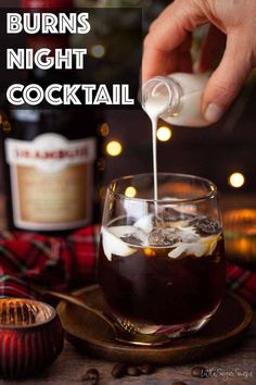 a person pouring drinks into a glass on top of a wooden table with christmas lights in the background