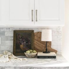 a white kitchen with marble counter tops and an art work on the wall behind it