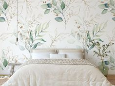 a white bed sitting next to a wall with green leaves on it