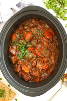 a pot filled with meat and carrots on top of a white table next to bread