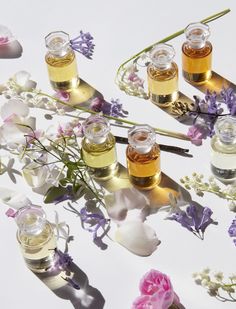 several small jars filled with different types of oils and flowers on a white tablecloth