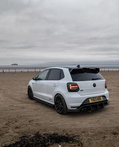 the rear end of a white car parked on top of a sandy beach next to the ocean