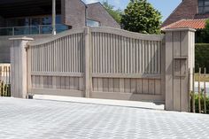 a large wooden gate on the side of a brick walkway next to a house and trees