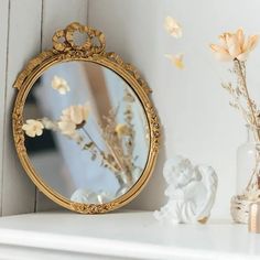 a mirror sitting on top of a white mantle next to a vase filled with flowers