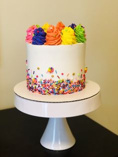 a white cake with sprinkles and rainbow frosting on top sitting on a table