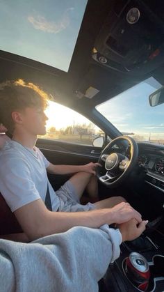 two people sitting in the driver's seat of a car, one is driving