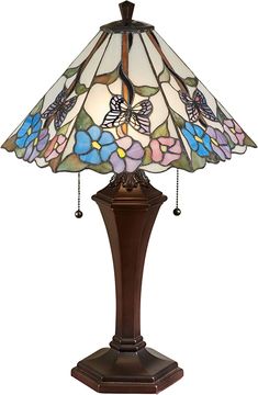 a lamp that is sitting on top of a wooden stand with flowers in the shade