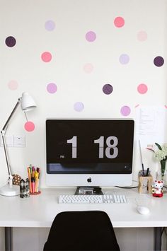 a white desk topped with a computer monitor next to a wall covered in pink and purple polka dots