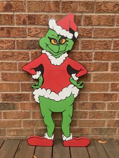 a wooden cutout of the grinch from the grinch movie standing in front of a brick wall