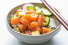 a bowl filled with salmon and cucumbers next to chopsticks