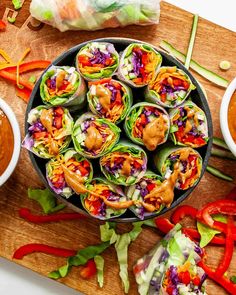 a wooden cutting board topped with lots of veggies next to bowls of dipping sauce