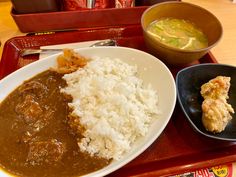 a tray with rice, meat and gravy next to a bowl of soup