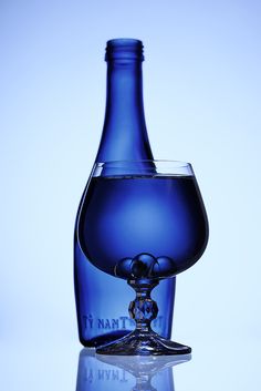 there is a blue wine glass next to a bottle