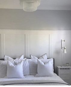 a bed with white pillows on top of it and a chandelier hanging from the ceiling