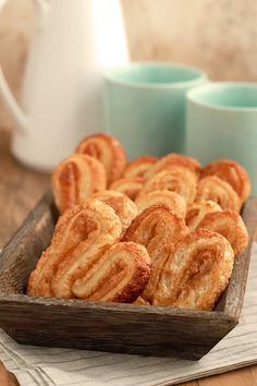 a wooden tray filled with cinnamon cookies on top of a table next to two mugs