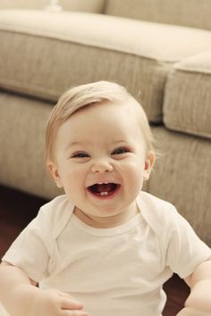 a smiling baby sitting on the floor in front of a couch