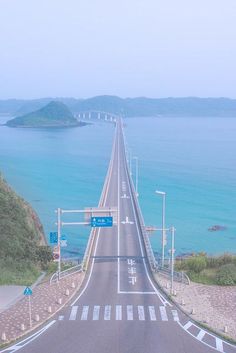 an aerial view of a highway near the ocean and bridge over water with mountains in the background