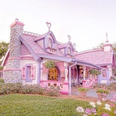 a pink and purple house sitting on top of a lush green field next to flowers