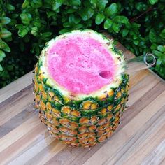 a large pineapple sitting on top of a wooden table next to green bushes and a pair of scissors